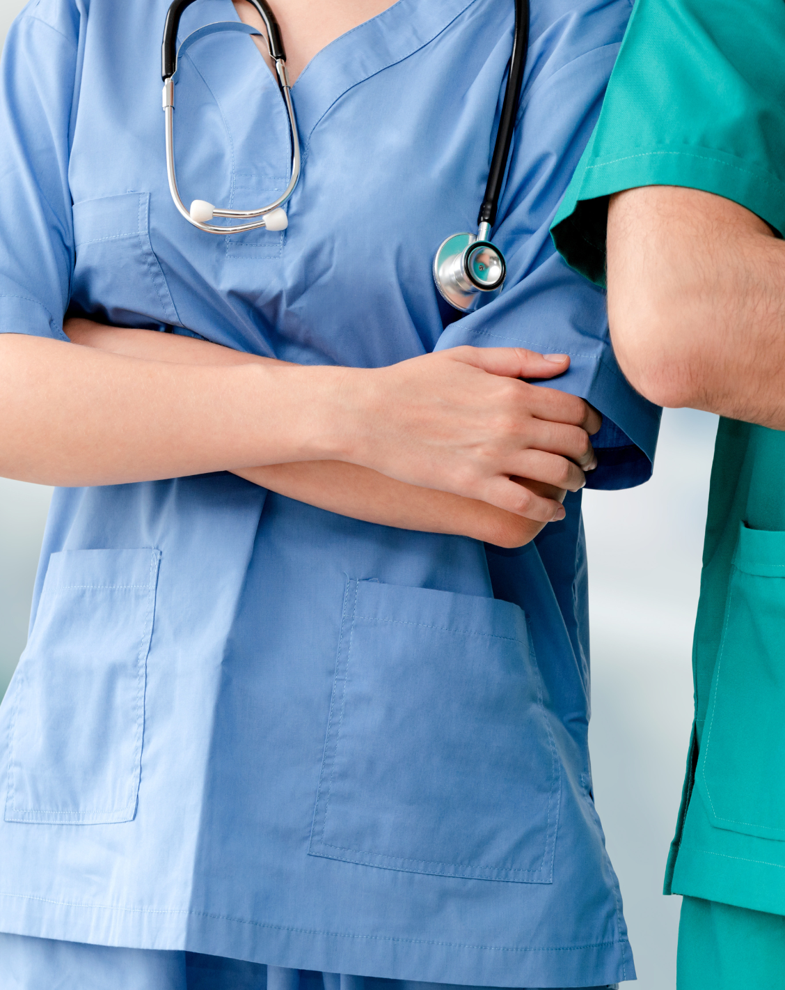 Image showing two healthcare professionals in scrubs, one with a stethoscope, arms crossed, standing confidently.