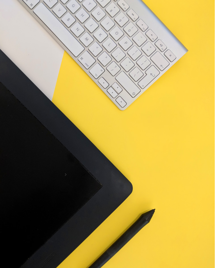 Top-down view of a graphic tablet, stylus, and keyboard on a yellow background, symbolizing creative work